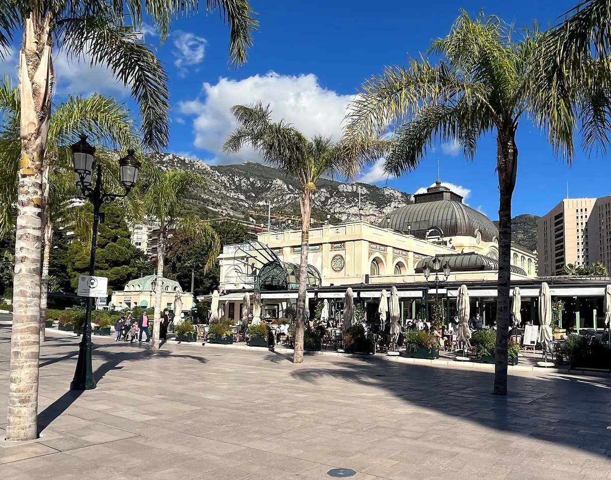 The pale domed facade of the Café de Paris with its terrace, seen across the paved square between tall palms