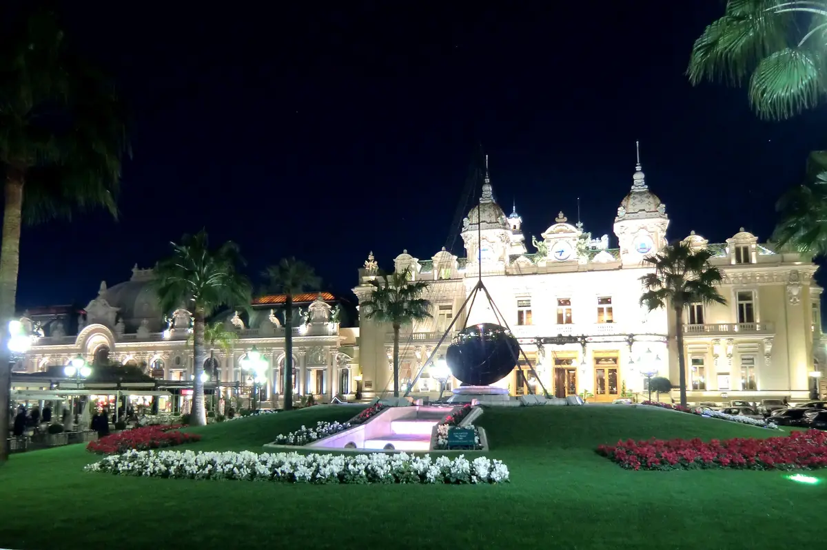 The Casino de Monte-Carlo floodlit at night, seen across its lawns and flower beds between palm trees