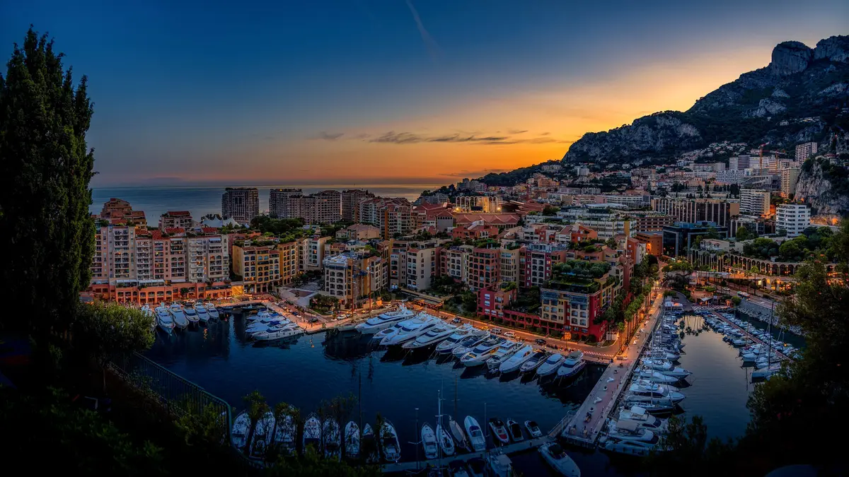 The harbour of Fontvieille at dusk, ringed by lit apartment buildings, with the hills behind