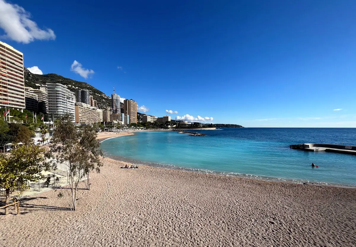 The curve of Larvotto beach with pale sand, clear turquoise water and tall apartment buildings behind