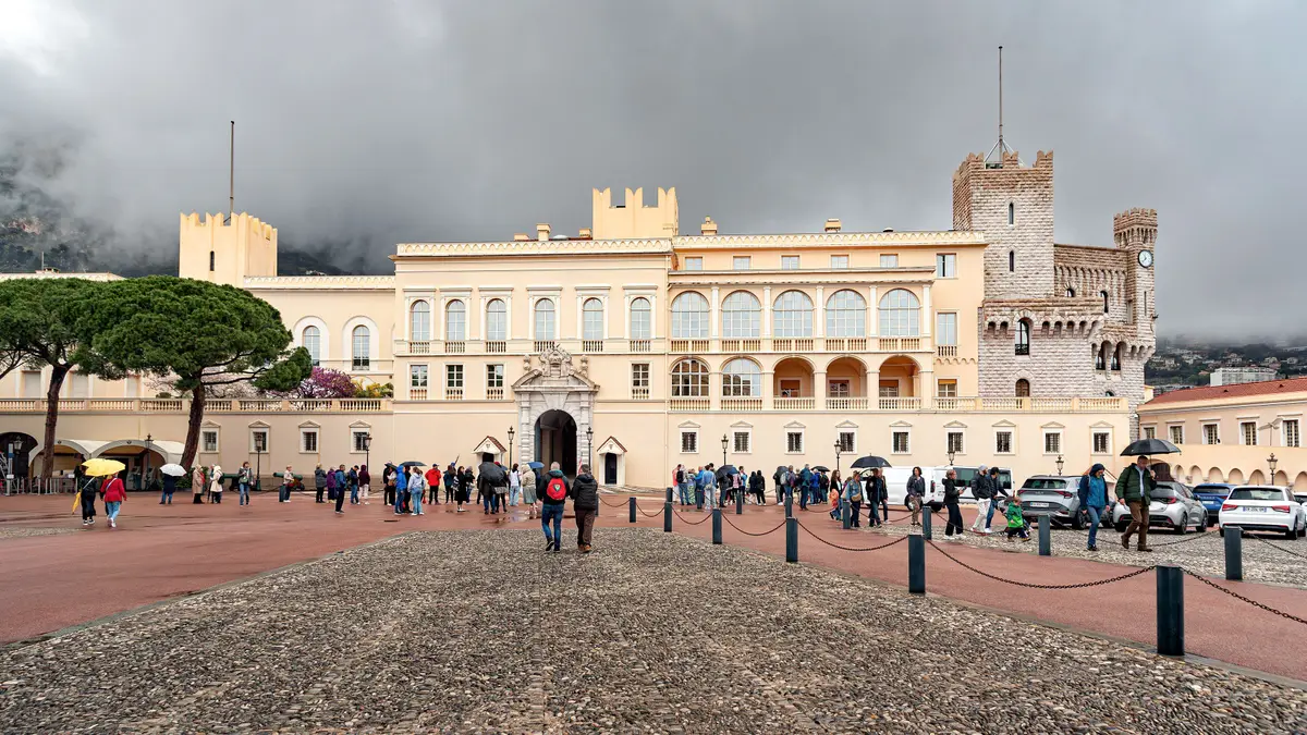 The pale facade and crenellated tower of the Prince’s Palace across a wide square, under low cloud