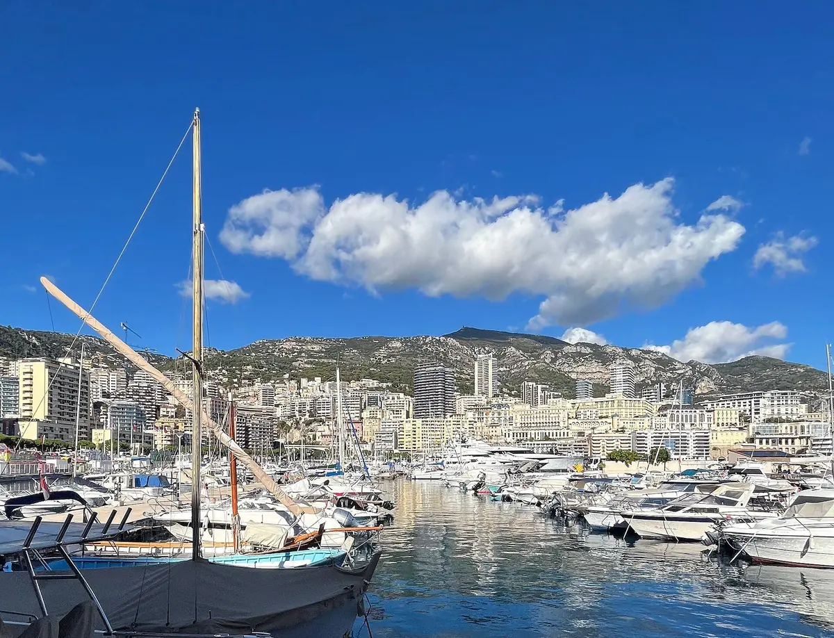 Moored boats in Port Hercule with a wooden mast in the foreground and the buildings of Monte-Carlo under a blue sky