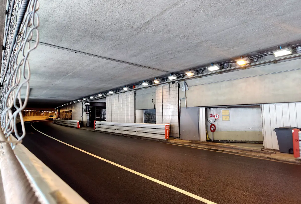 The curving road tunnel of the Grand Prix circuit, lit by a row of ceiling lights, with safety fencing in the foreground
